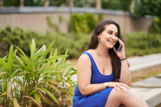 Woman in a blue dress talking on the phone outside.