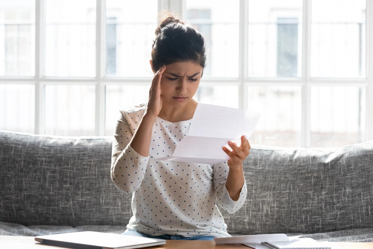 Woman looking worried while sitting on couch and reading a water bill