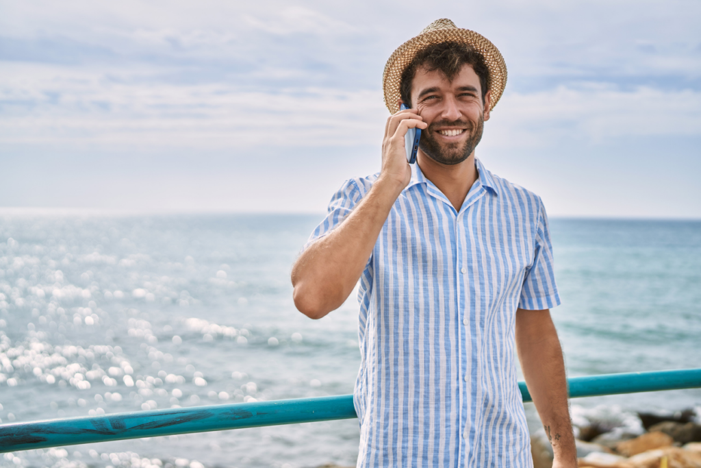 A young man at the beach talking on a cell phone.